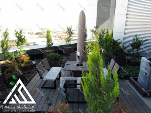 طراحی فضای سبز تراس کرج پس از اجرا شامل فلاورباکس گل درخت گلدان چتر و میز و نیمکت محوطه و آبنما راهروی چوبی